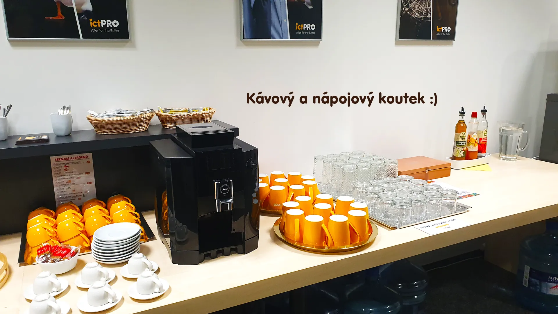 Kávový koutek s automatickým kávovarem, žlutými a bílými hrnky, sklenicemi a sirupy.