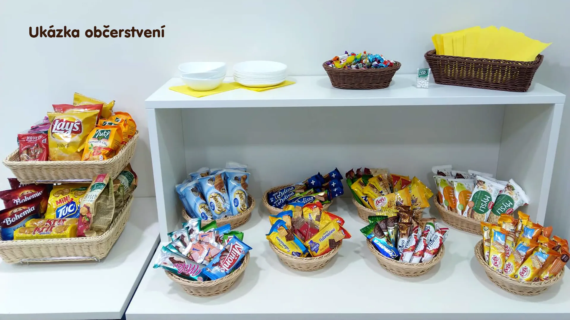 Proutěné košíky naplněné balenými slanými snacky, sladkými sušenkami a tyčinkami.