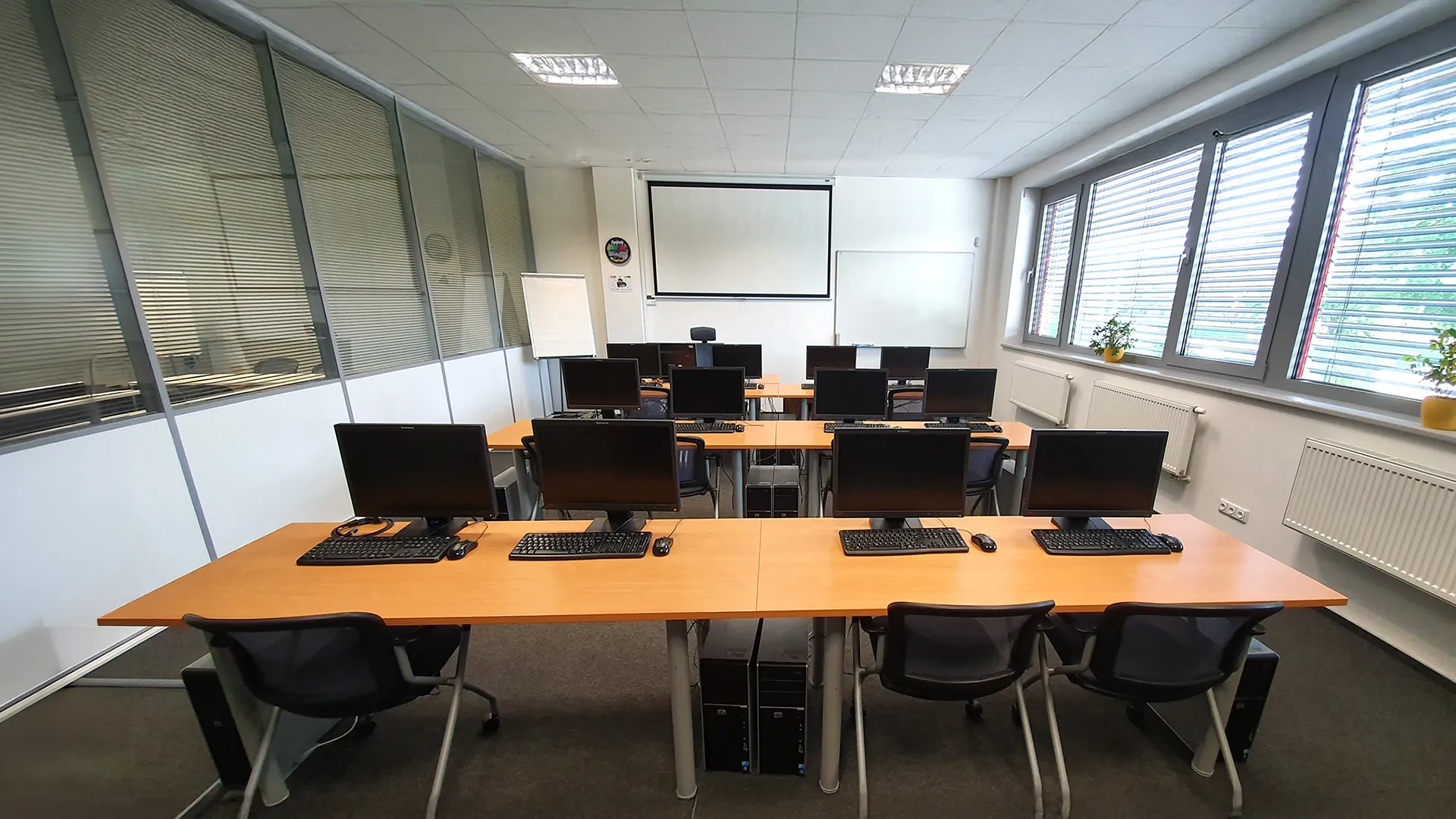 IT učebna se stoly, počítači s monitory a projekčním plátnem v přední části místnosti.